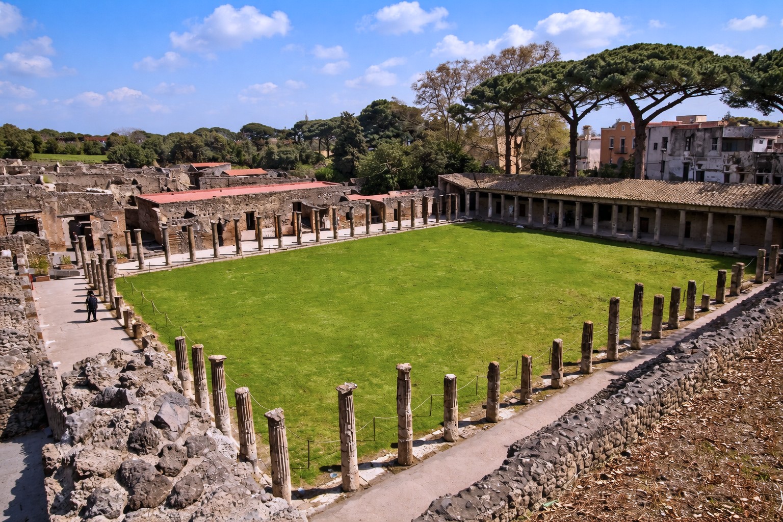 Quadriportico dei Teatri in Pompei mit großem rechteckigem Innenhof, umgeben von Säulenhallen, Blick über die Rasenfläche auf die antiken Mauern und Pinien im Hintergrund