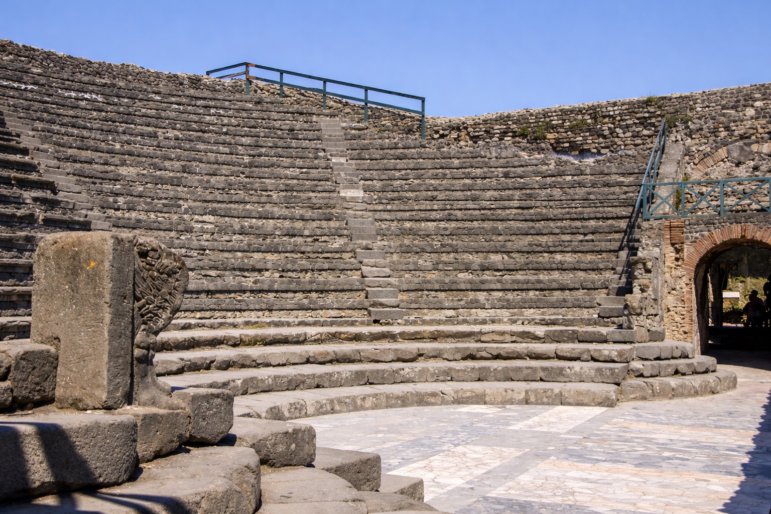 Odeion von Pompei mit halbrundem Zuschauerraum aus steinernen Sitzreihen, Blick von der Orchestra auf die ansteigenden Ränge und die erhaltene Umfassungsmauer unter klarem Himmel