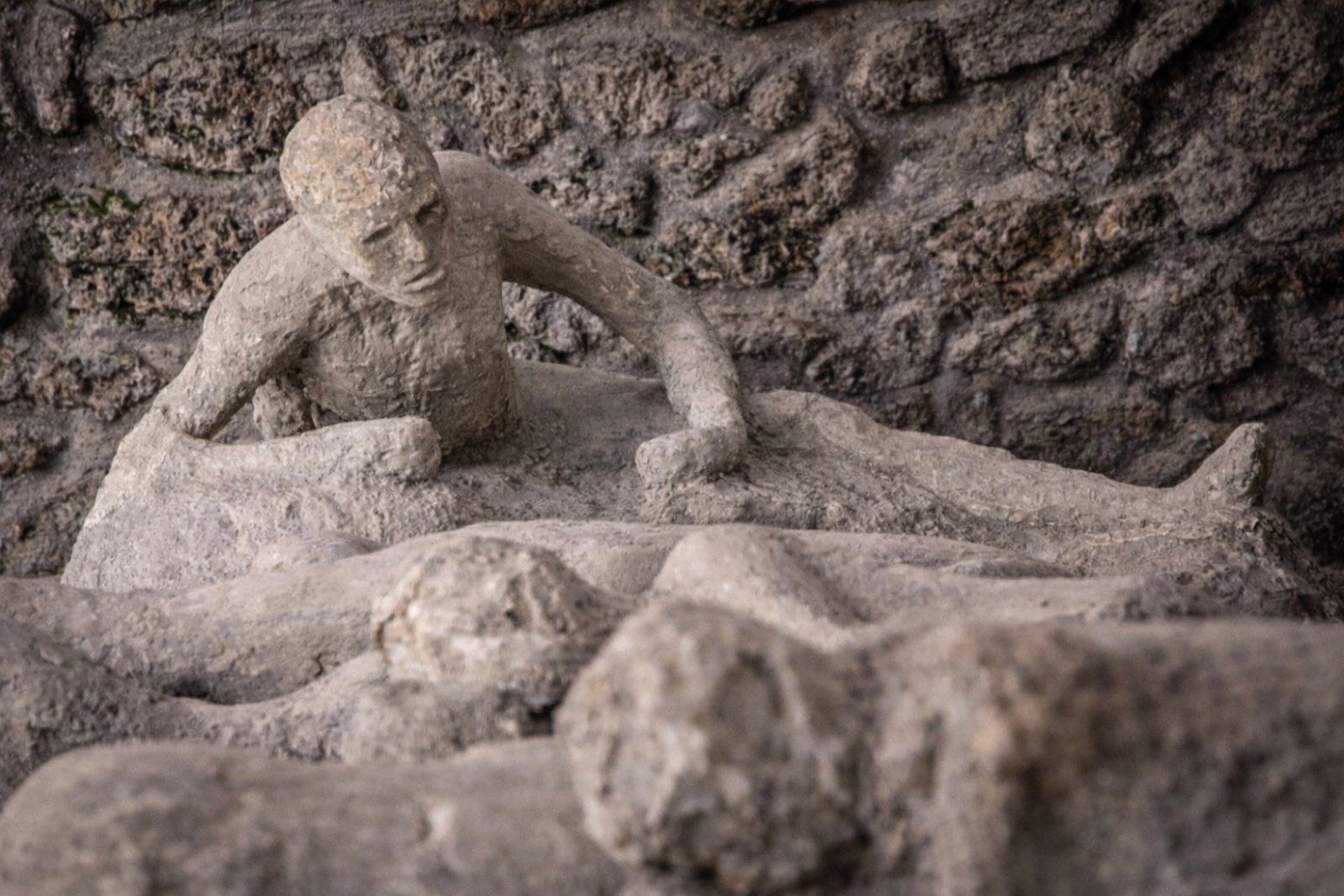 Gipsabdruck eines Opfers im Orto dei Fuggiaschi in Pompei, liegende menschliche Figur vor einer antiken Steinmauer, die die letzten Momente während des Vesuvausbruchs zeigt