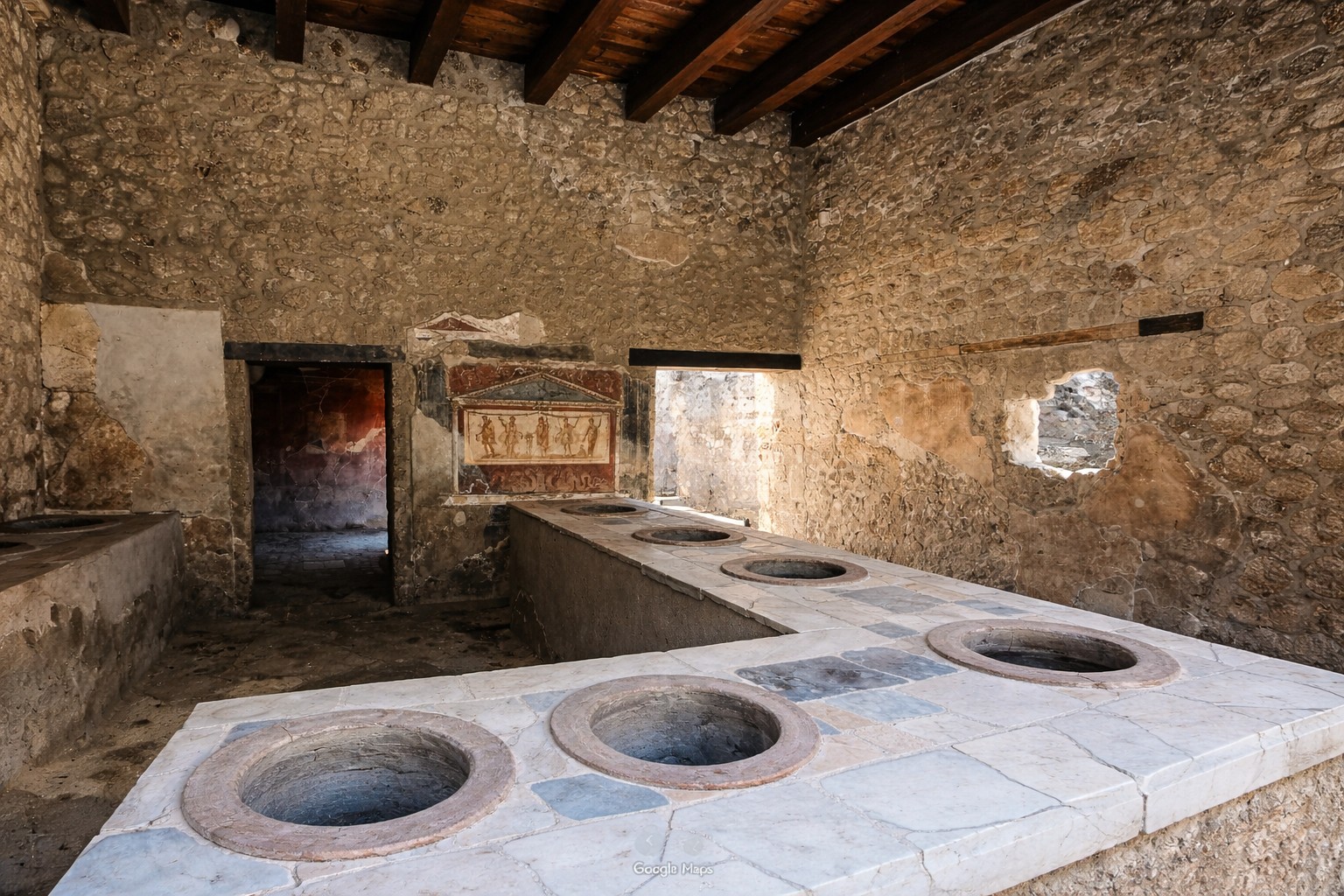 Thermopolium von Pompeji mit steinerner Verkaufstheke, runden eingelassenen Vorratsgefäßen, erhaltenen Wandmalereien und Blick in den antiken Schankraum